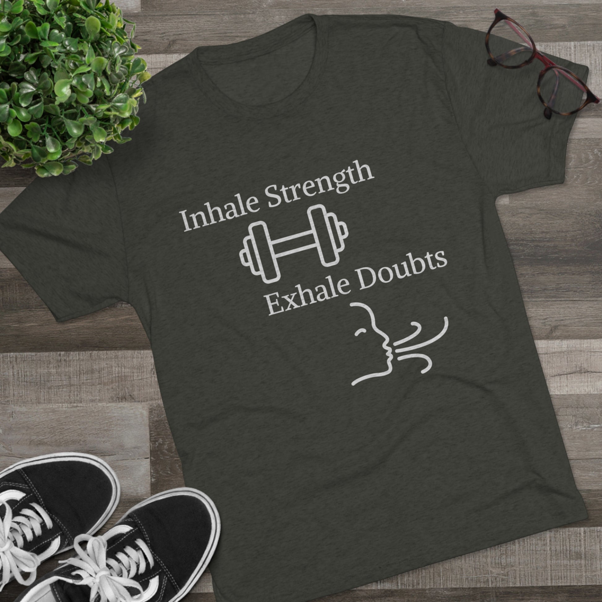A charcoal gray workout apparel t-shirt on a wooden floor with the Inhale Strength Exhale Doubt w Images - Unisex Tri-Blend Crew Tee by Printify, and accompanying sneakers and glasses.