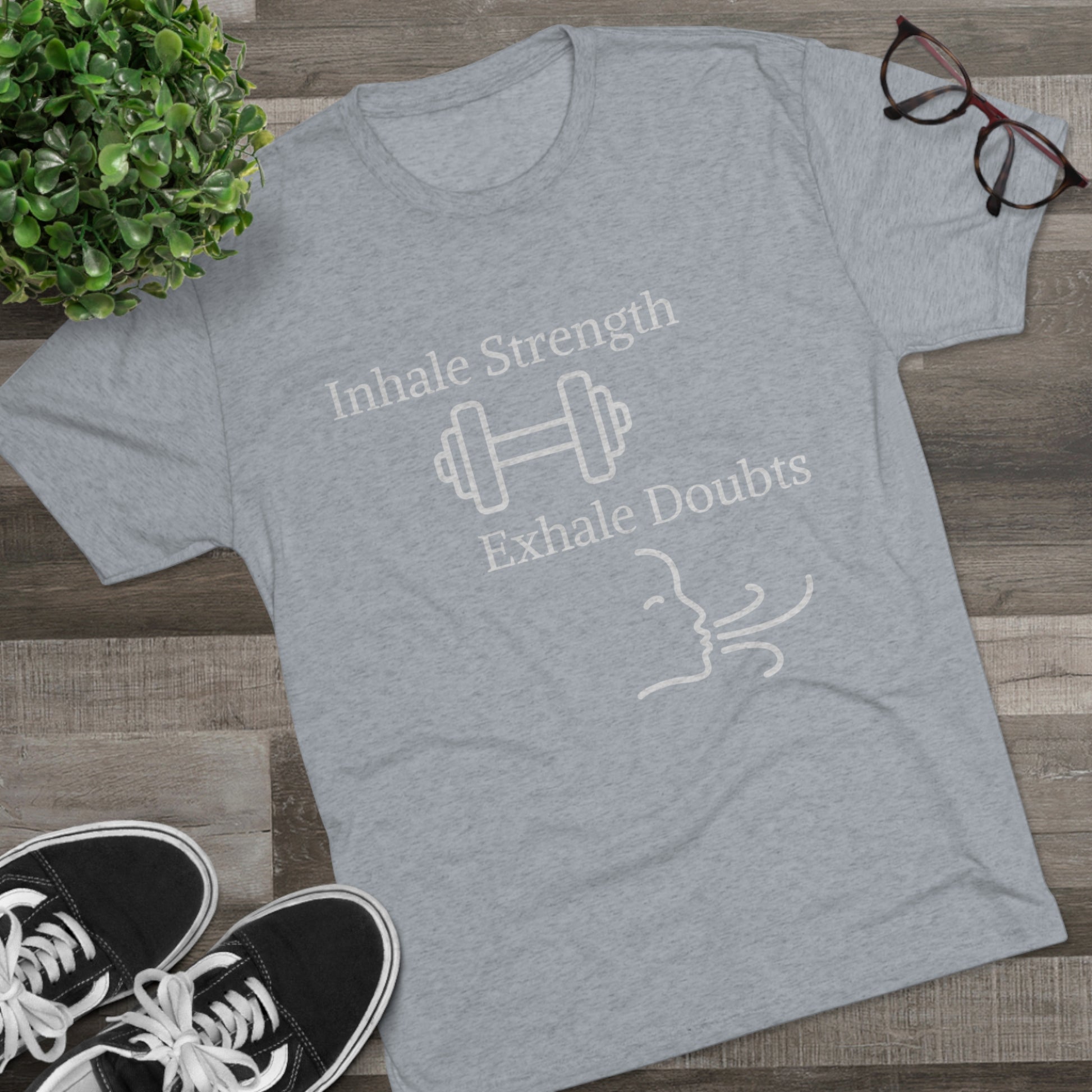 Blue Inhale Strength Exhale Doubt w Images - Unisex Tri-Blend Crew Tee by Printify displayed on a wooden floor with sneakers and glasses beside it.