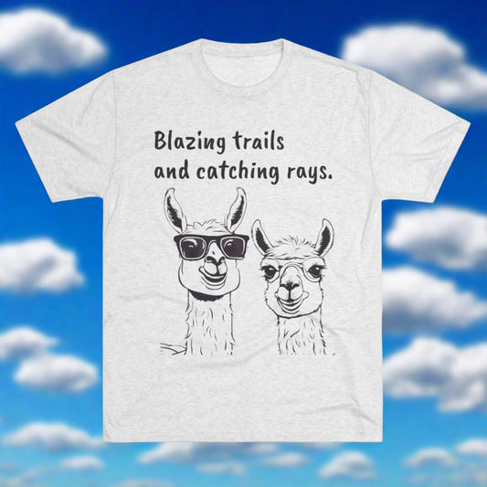 A light gray “Blazing Trails Llama - Tri-Blend Crew Tee - Unisex Fit” from Printify, available at Blue Sky Runners store, features two hand-drawn llamas. The llama on the left sports sunglasses, while the one on the right has a neutral expression. Above them, "Blazing trails and catching rays" is written against a backdrop of fluffy clouds.
