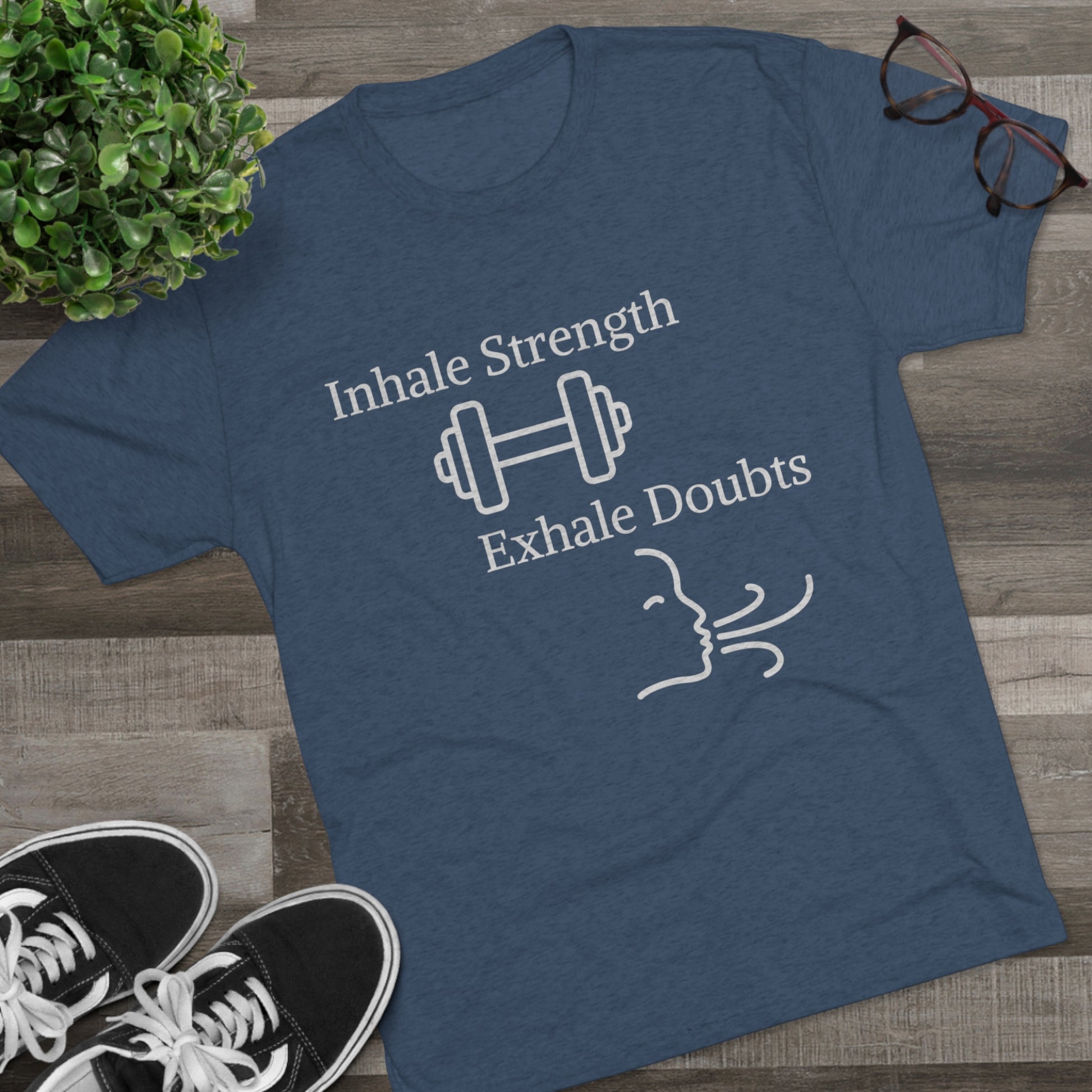 A Printify Inhale Strength Exhale Doubt w Images - Unisex Tri-Blend Crew Tee with the motivational text "inhale strength exhale doubts" and an icon of a dumbbell and wind graphic, displayed on a wooden floor next to Blue Sky Runners sneakers.