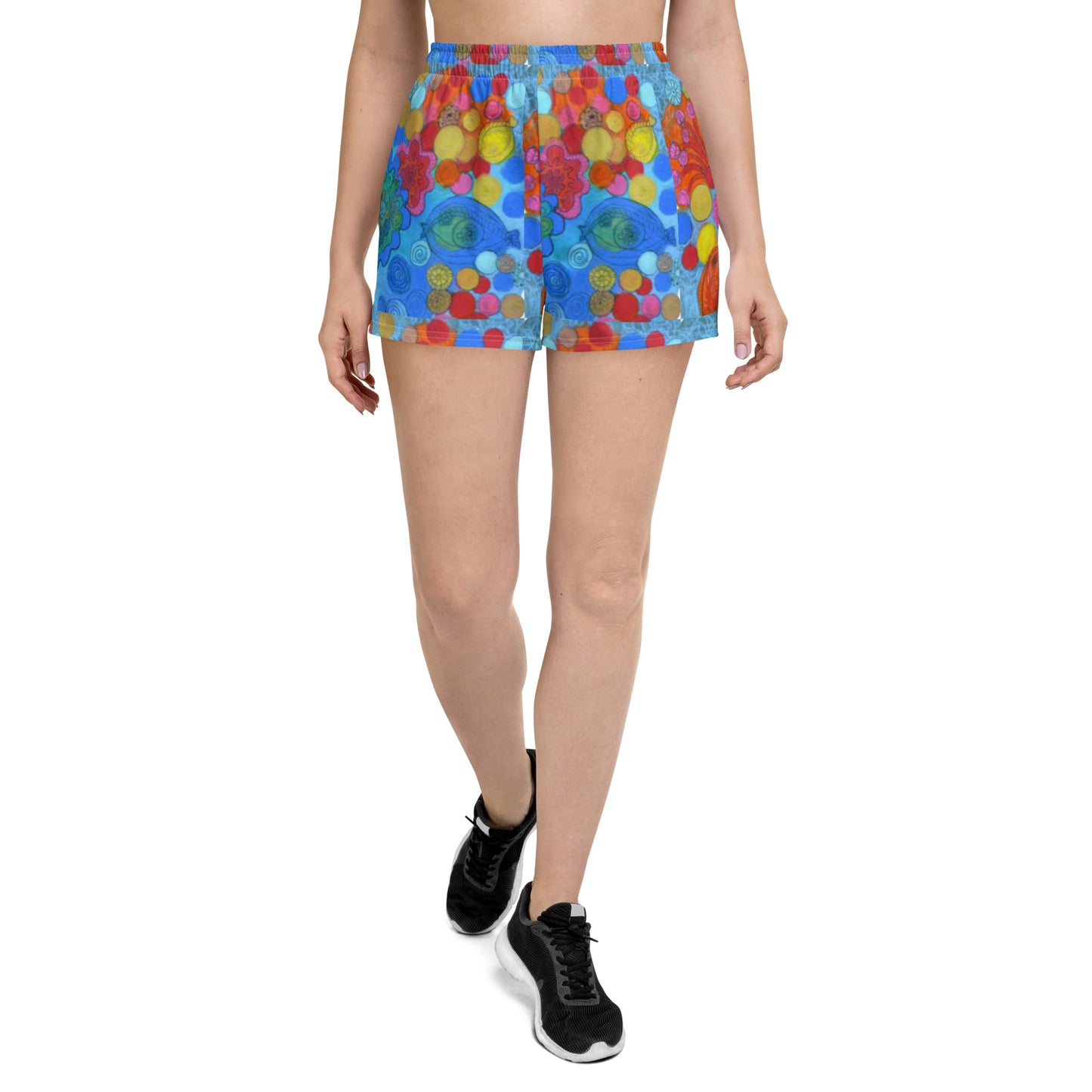 A person is wearing Blue Sky Runners' Coral women’s recycled athletic shorts, adorned with a vibrant, abstract pattern featuring eyes and various colorful shapes such as circles and flowers. They are walking forward, and their black athletic shoes are visible against the plain white background.