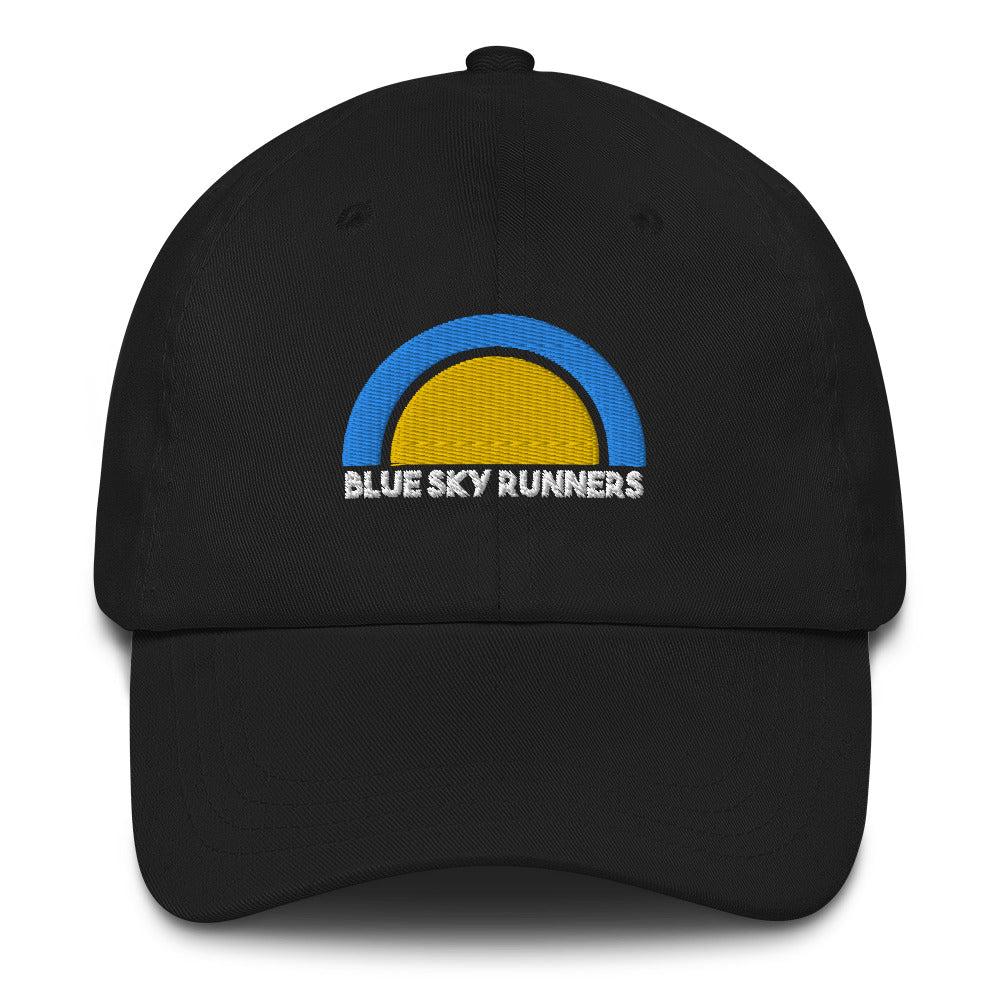 The Blue Sky Runners Dad Hat is a black low profile cap with a logo featuring a yellow semicircle enclosed by a blue arc above the words "Blue Sky Runners" in white text on the front. It includes a curved brim and an adjustable strap at the back.