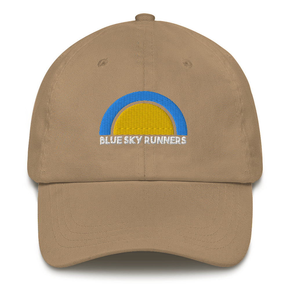 The Blue Sky Runners - Dad Hat, from the brand Blue Sky Runners, is a khaki low profile cap featuring a blue and yellow semicircular logo above the embroidered text "BLUE SKY RUNNERS" in white. It also has a curved brim and an adjustable strap at the back.