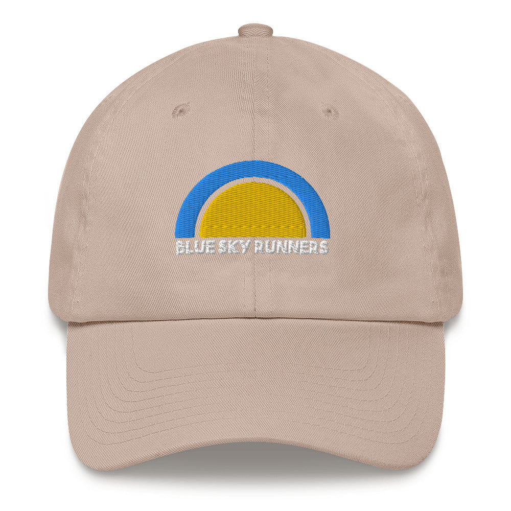 The Blue Sky Runners - Dad Hat by Blue Sky Runners is a beige, low-profile hat featuring a blue and yellow semi-circle design on the front with "Blue Sky Runners" in white text below, and an adjustable strap for a perfect fit.