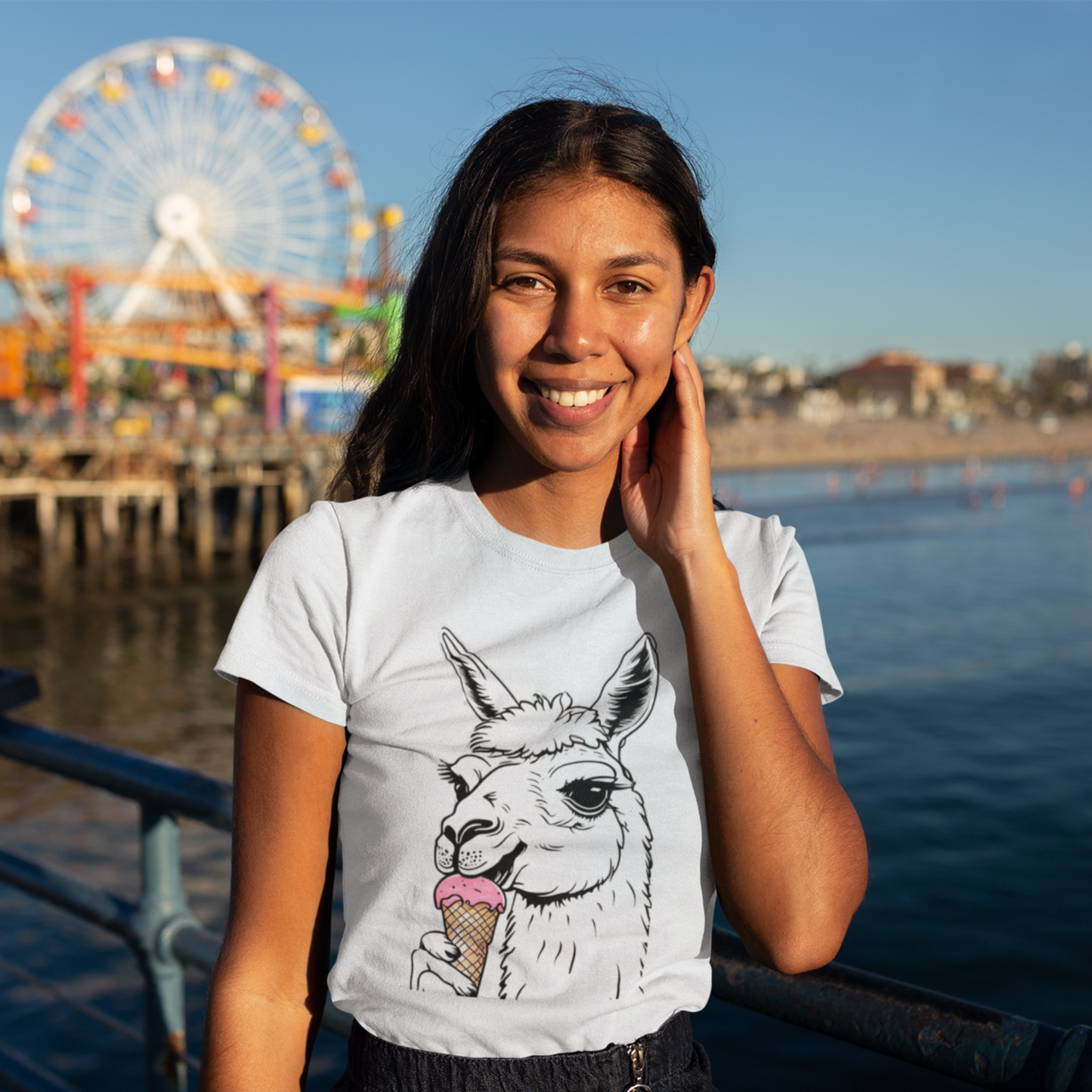 A smiling woman in late afternoon sun, wearing a t-shirt with an ice cream cone eating Llama design, on the santa monica pier